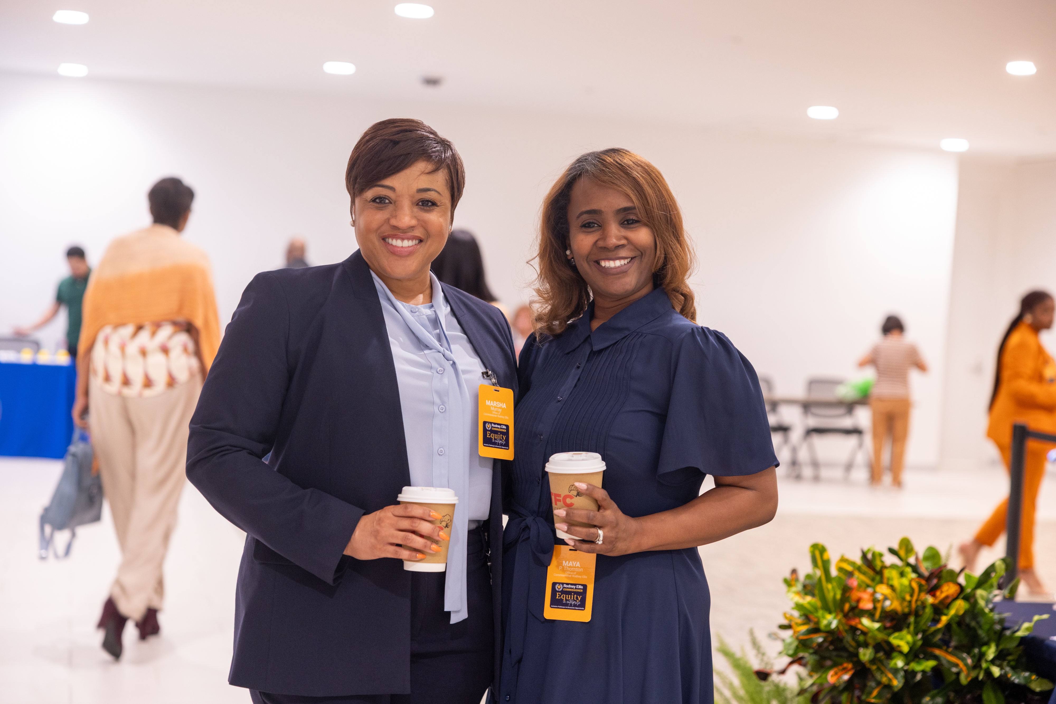 Two attendees networking and smiling, holding coffee cups, wearing Equity in Enterprise badges